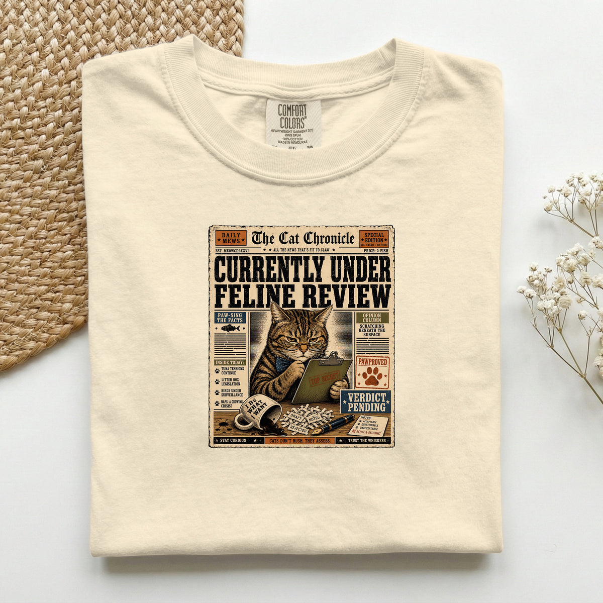 Currently Under Feline Review graphic tee in Ivory, folded mockup