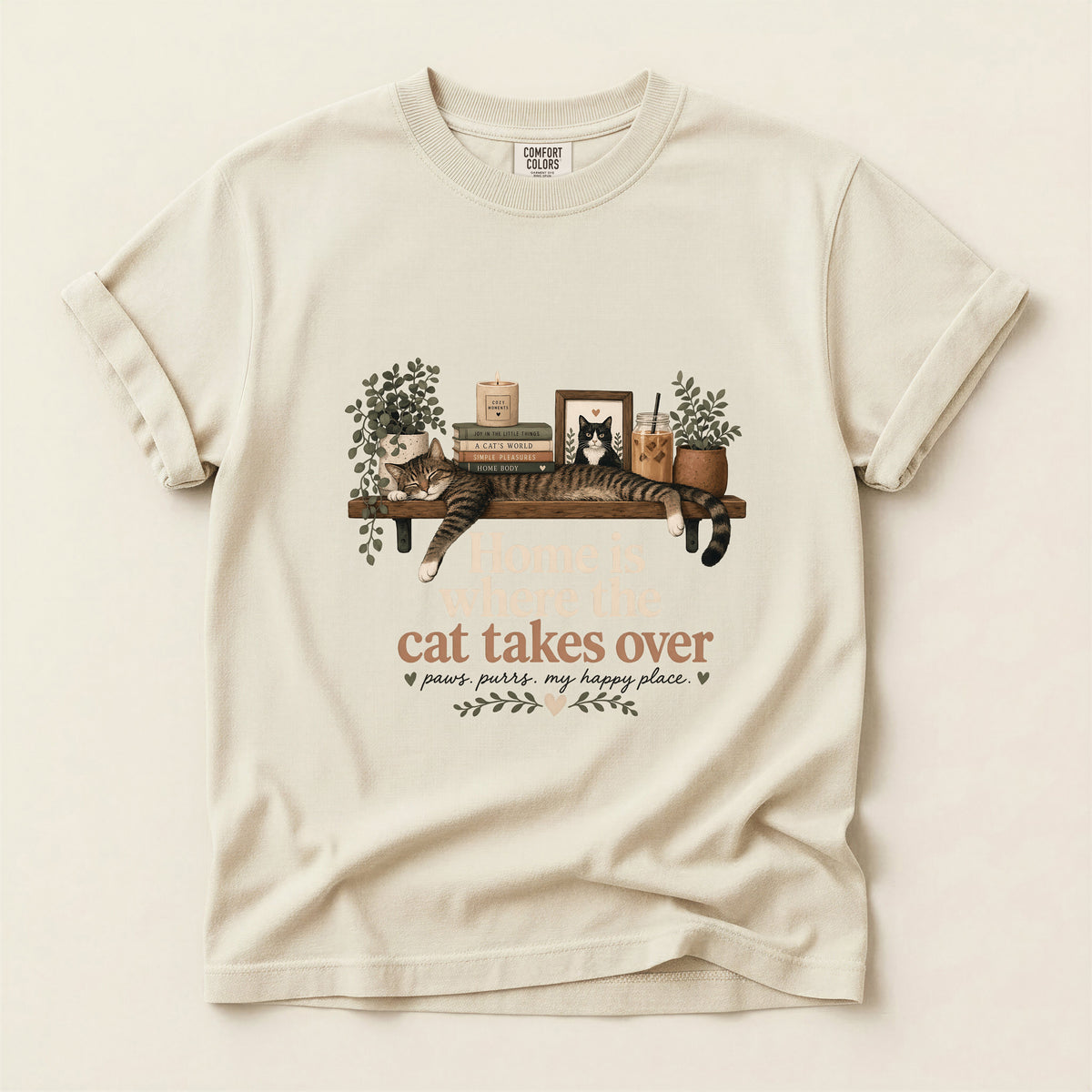 An off-white short-sleeve t-shirt with a graphic of a cat stretching on a wooden shelf, accompanied by the text 'cat takes over' and smaller decorative text below, displayed flat against a matching off-white background.