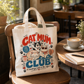 Cat Mum Club tote bag propped on wooden chair in cafe